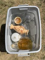 Top down view of a white bin containing an assortment of glass and ceramic items including two clear glass bowls, speckled ceramic jug, white decor piece, amber and clear glasses.