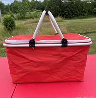 Side view of the red insulated cooler bag showing rectangular shape, white zipper, and dual support handles in folded-up position.