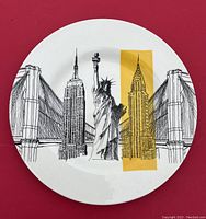 Top-down view of the Royal Stafford ceramic plate showing New York City landmark illustrations including Brooklyn Bridge, Empire State Building, Statue of Liberty, and Chrysler Building with yellow highlight.