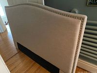 Front view of beige upholstered headboard showing curved top and black base.