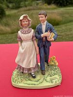 Figurine of young man and woman in vintage clothing with grass and flowers on base, viewed from front and angled.
