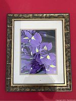 Framed art print showing vivid purple iris flowers. The gold and black decorative frame and white matting are visible.