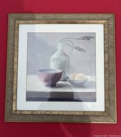 Framed art showing a simple still life of a jug, bowls, and eggs on a muted background with gold-tone chunk framed edge