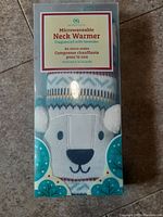 Front view of packaged microwaveable neck warmer showing the product branding and animal face design on fabric.