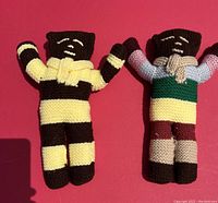 Two hand knitted dolls with striped and multicolor yarn shown on red background