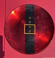 Photo of a red glass charger plate with a black vertical stripe and gold square belt buckle design mimicking a Santa Claus belt.