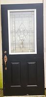 Front view of black exterior door with large decorative glass panel and brass handle.