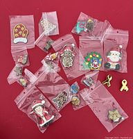 Variety of Christmas-themed pins and ornaments individually packaged in small plastic bags on red background.