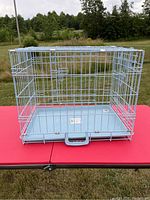 Blue metal wire pop up pet kennel with front door and plastic base on outdoor red table.