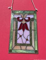 Full view of rectangular stained glass panel featuring green borders, red flower petals, light purple background, and beige highlights. Hanging wire attached for display.
