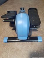 Blue and black compact stepper from side angle, showing foot pedals and central unit.