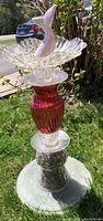 Photo of an upcycled birdbath outside showing glass and ceramic components, decorative stone base, and pastel pink mermaid tail accent.