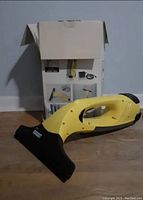 Kärcher WV 50 window vacuum cleaner handheld device on floor with box behind it.