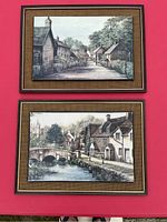 Photo showing two framed pictures portraying English countryside village scenes with burlap matting and dark frames.