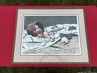 Photo showing framed country kitchen style picture of apples in basket spilled on quilt with cup and garlic on wooden surface.