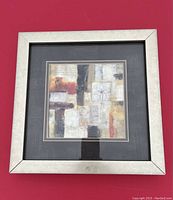 Framed picture with abstract floral design in light gold frame on black mat with orange, yellow, beige, black, and white colors