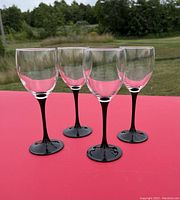 Photo showing set of four wine glasses with clear bowls and black stems on a red surface outside.