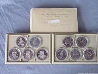 Overview photo showing 10-piece Indian Heritage medallion set in protective capsules inside two beige trays with outer box on top featuring handwritten descriptions and notes.