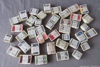 Photo showing 40 bundles of Canadian postage stamps wrapped in paper bands with handwritten labels indicating approximate catalogue number and year (1950s-1960s).