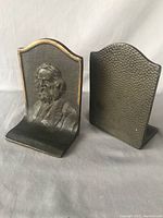 Pair of heavy metal bookends showing front with raised profile of a bearded man on textured backdrop.