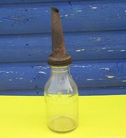 Full view of the clear glass oil bottle with rusted metal spout against blue background.