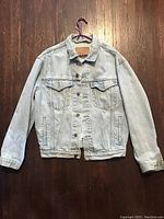 Front view of Levi's stonewashed denim jacket on hanger showing button front, chest pockets, and collar.