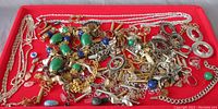 Wide view of assorted jewelry making components mixed on a red background including chains, beads, charms.