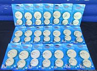 Full view of all 21 unopened packages of sink drain stoppers arranged on a surface, showing two different sizes in blue packaging.