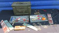 Photo of military ammo box and two trays with fishing equipment spread around
