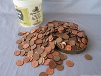 Coins spilled from a Captain Black round container and lid for scale, showing a large quantity of pennies with varying copper tones.