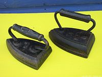Pair of heavy cast iron sad irons on yellow surface showing size and handle design
