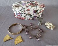 Photo showing oval fabric covered trinket box with floral pattern alongside assorted jewelry and a thimble