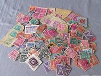 Overhead image showing a large assortment of used USA postage stamps mostly detached from paper, various colors and designs.