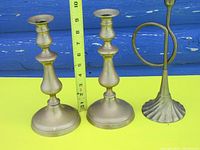 Three brass candlesticks: two matching baluster style and one unique fluted base with ring handle, showing size with ruler for scale.