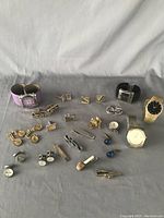 Assorted watches, cuff links, and tie clips arranged on gray surface