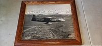 Framed black and white photo of military jet flying over landscape with mountains visible.