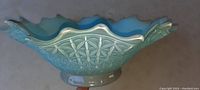 Side view of the heavy glass bowl showing blue tint, fluted scalloped edges, and intricate floral geometric exterior pattern.