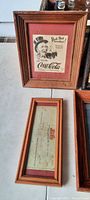 Wood-framed Coca-Cola vintage ad with a man in a hat and a framed Pepsi-Cola company check dated 1947.