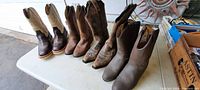 Four pairs of ladies cowboy boots displayed side by side on white table, showing side profiles and overall condition.