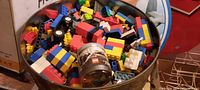Metal 5 gallon can filled to the top with assorted colorful LEGO bricks and pieces with varied shapes and sizes, including some wheels and a small LEGO branded container inside.