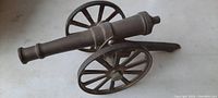 Side angle view showing the brass barrel and steel carriage with wheels on a white surface.
