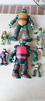 Eight Ninja Turtle figures arranged on surface including two large 8-inch figures and six smaller figures in various colors and accessories.