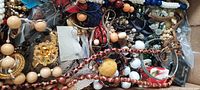 Flat box view of mixed costume jewelry showing various necklaces, earrings, bracelets, and brooches with beads and metal components.
