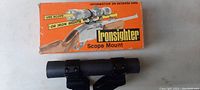 Black metal scope mount placed in front of original vintage orange and white Ironsider box showing usage instructions.