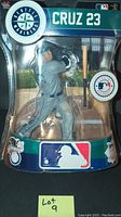 Front view of Nelson Cruz baseball figurine in packaging, showing Seattle Mariners gray batting uniform and separate bat accessory