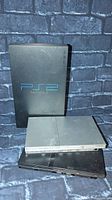 Three PlayStation 2 consoles stacked, showing front and top sides with logos and buttons visible.