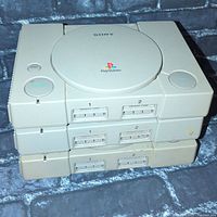 Three Sony PlayStation 1 consoles stacked showing front memory card slots, controller ports, power and open buttons
