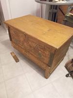 Front and side view of wooden chest showing floral paint detail and detached leg on floor.