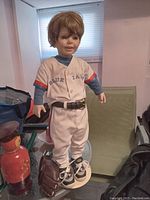Full body view of the porcelain figurine dressed in Blue Jays baseball uniform standing on beige base, holding brown glove.