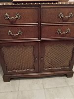Front view of antique wooden cabinet showing four drawers with brass handles and two fabric paneled doors below.